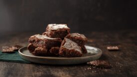 Slices Homemade brownie cakes with dark chocolate sprinkled with icing sugar on a dark background.